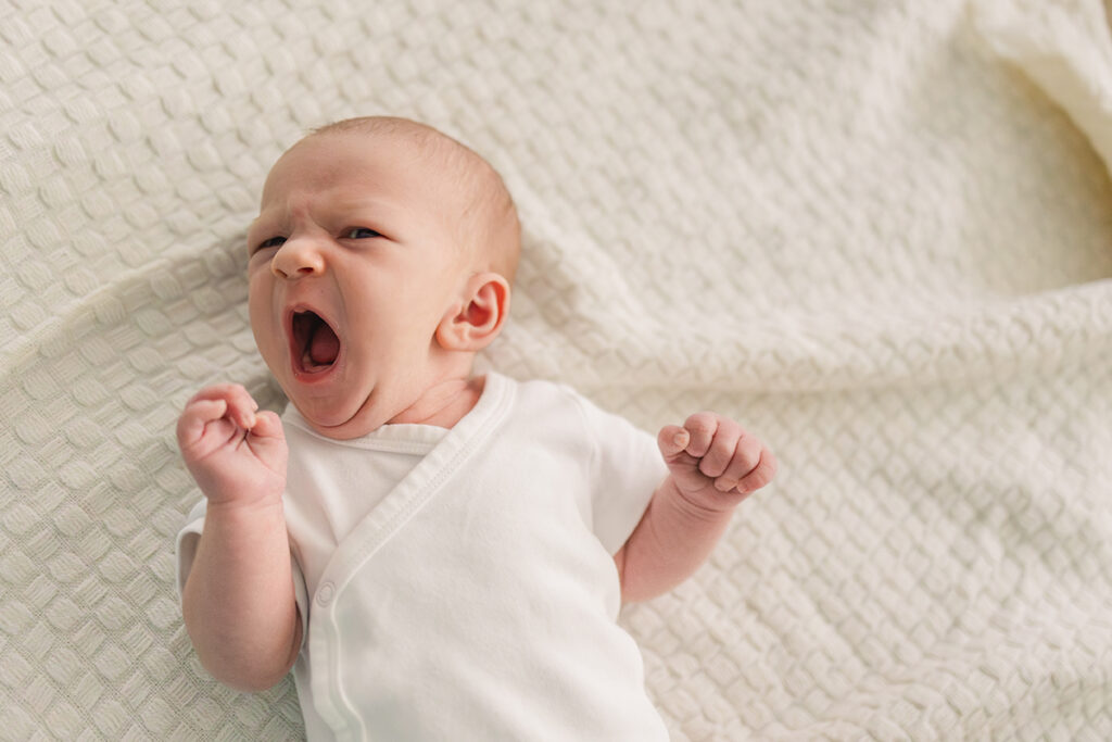 a baby lying on a blanket yawning