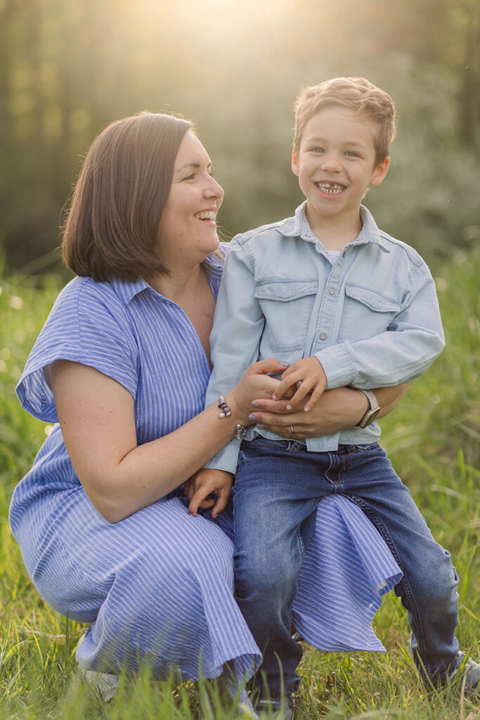 Mutter kniet und ihr Sohn sitzt auf dem Fuss in der Natur bei einem Familienshooting