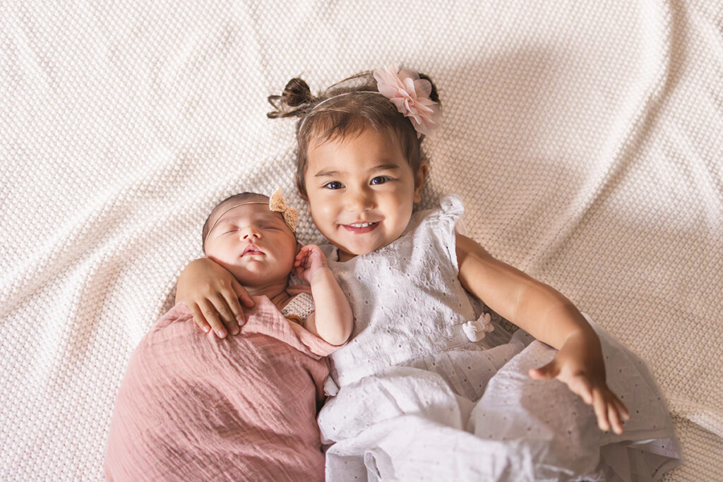 Baby und Schwester liegen auf einer Decke