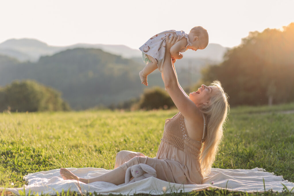 Mutter hebt ihr Baby in die Luft bei Sonnenuntergang